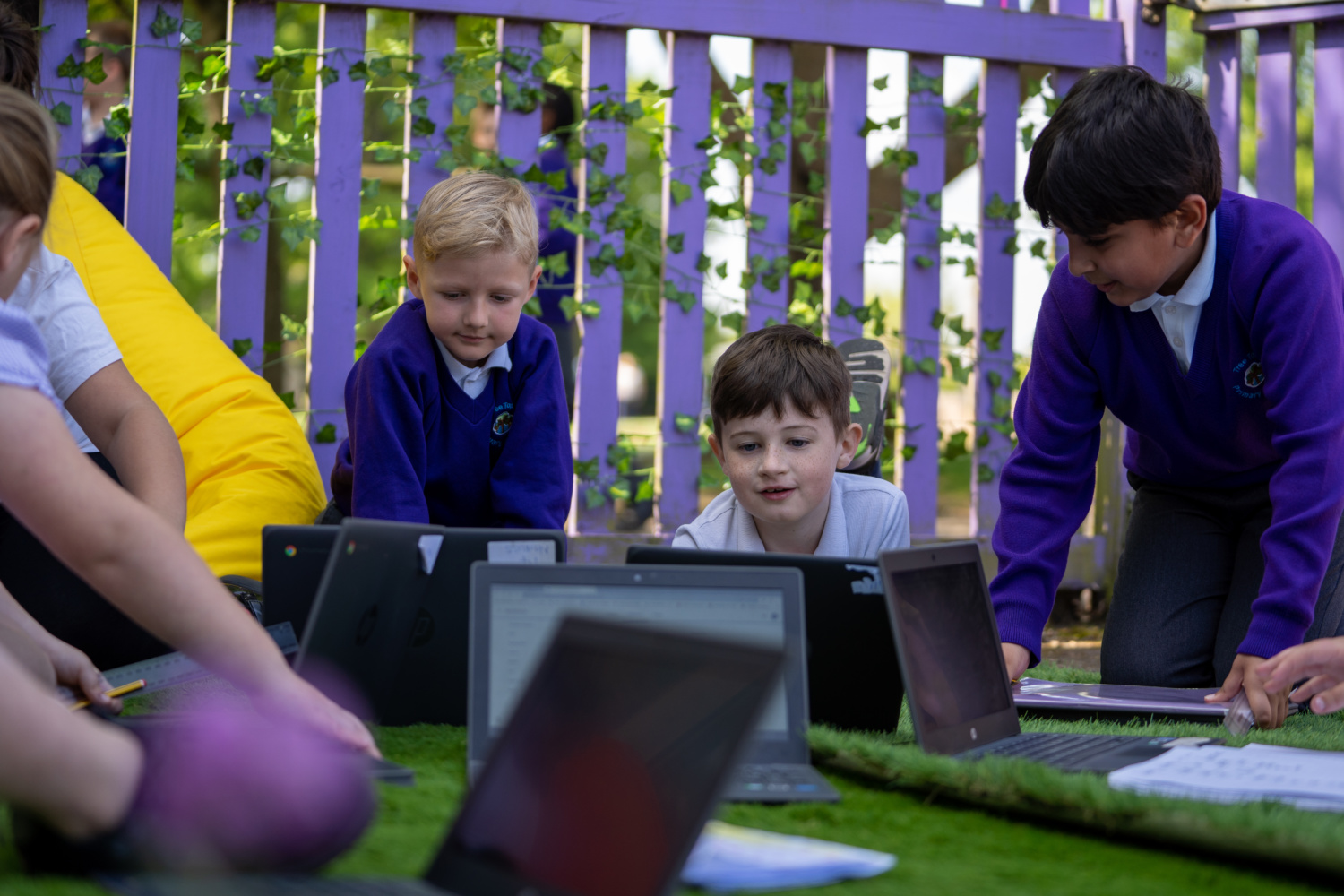 A small group of Tree Tops pupils are seen working on their laptops together, outdoors on the school grounds.