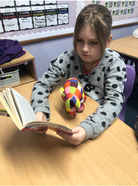 Student sat reading with Elma the elephant