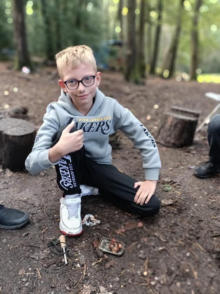 A child crouching in the forest with their thumb up