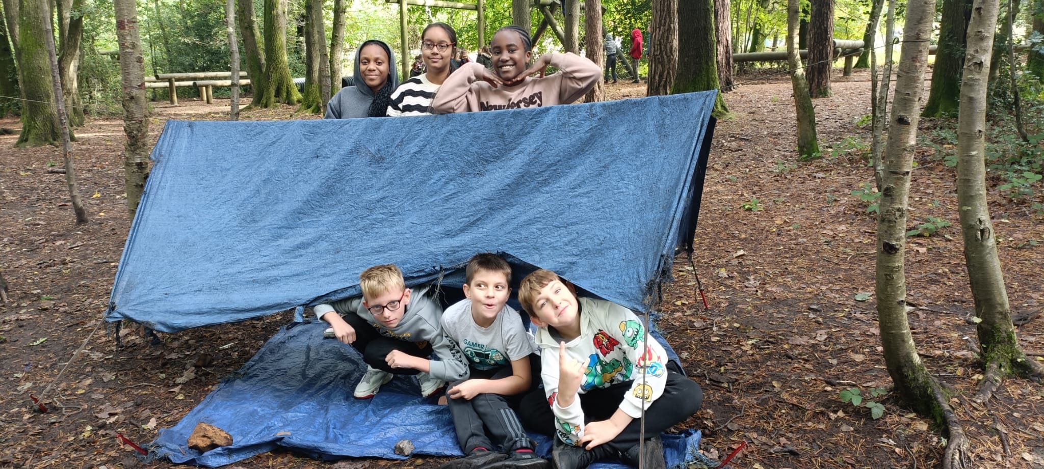A group of students sitting under a piece of tarpaulin in the woods