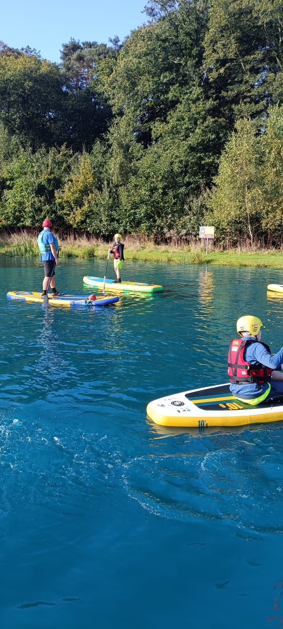 Several students standing and kneeling on paddle boards on a lake