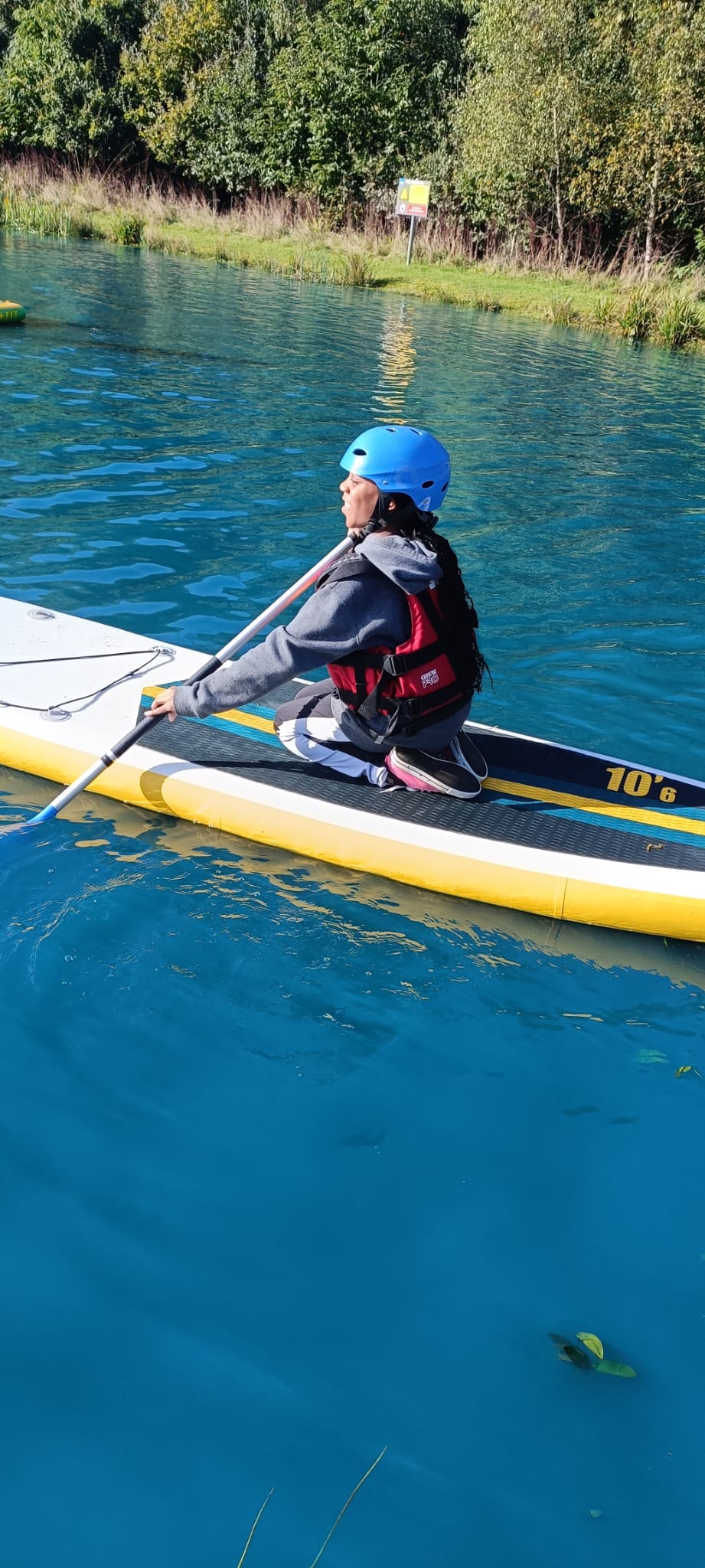 A student kneeling on a paddle board, smiling