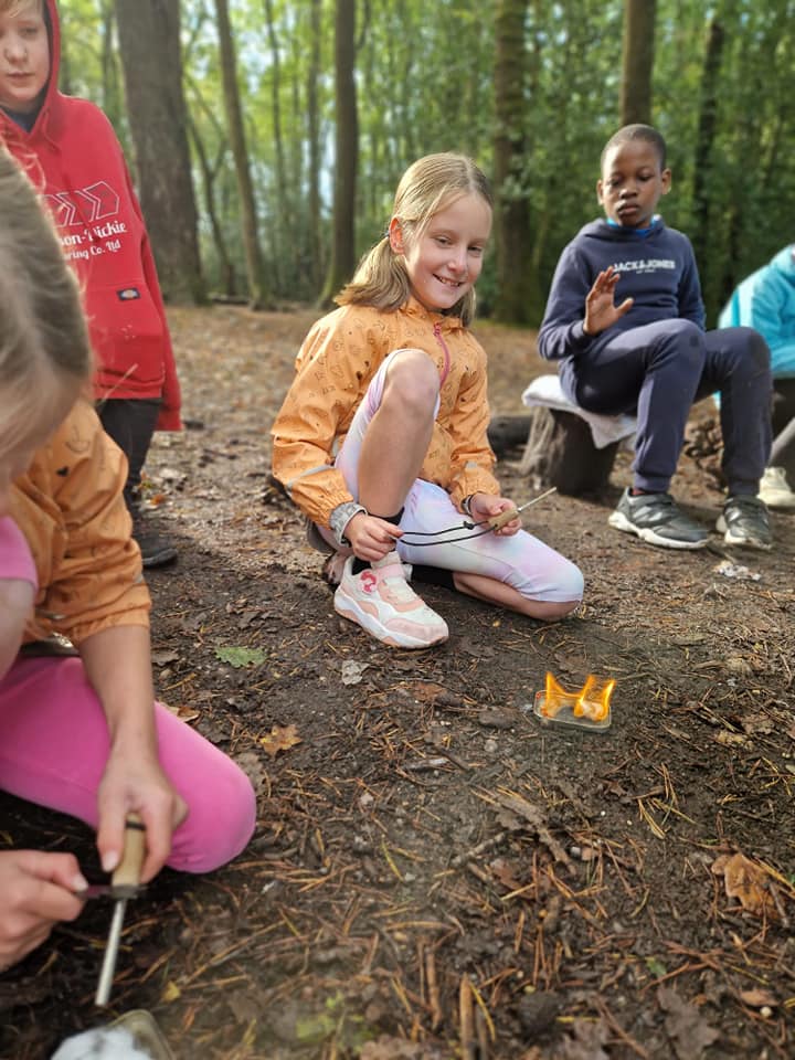 A child smiling for a photo in front of a small flame on the forest floor