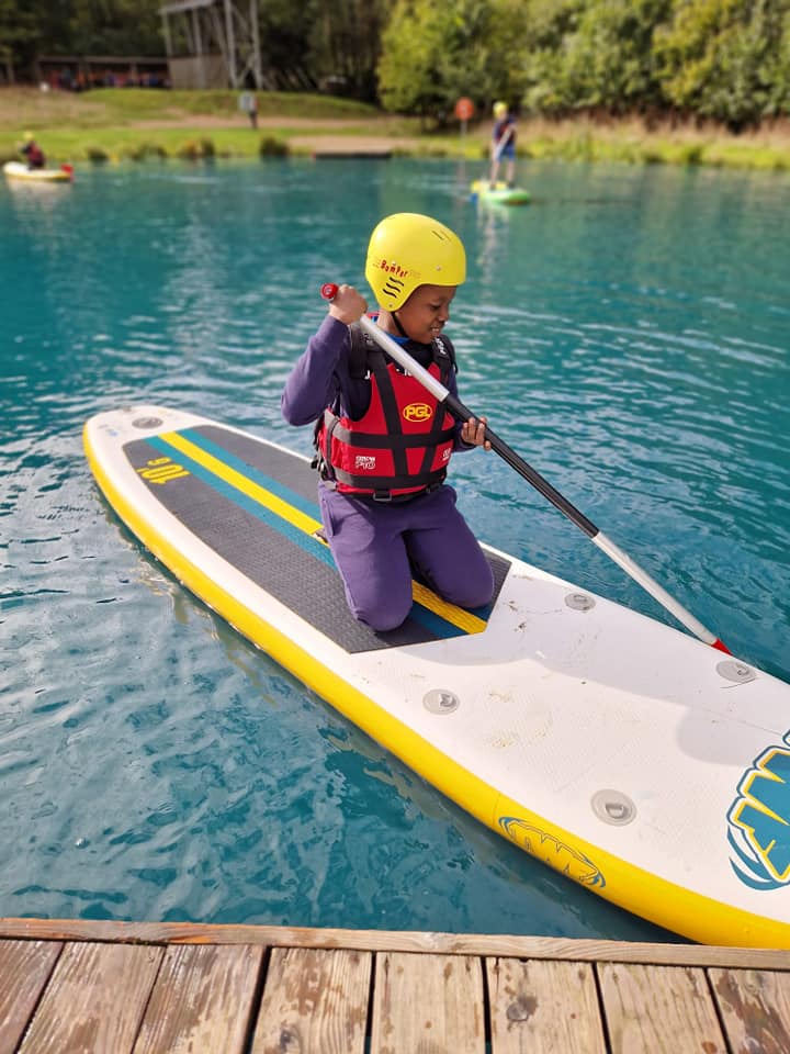 A student kneeling on a paddle board, smiling