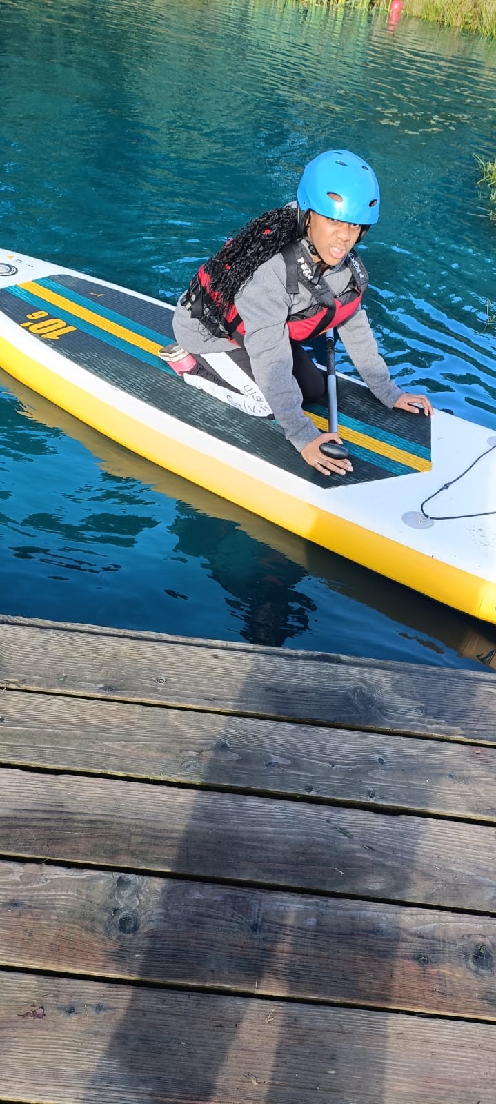 A student kneeling on a paddle board