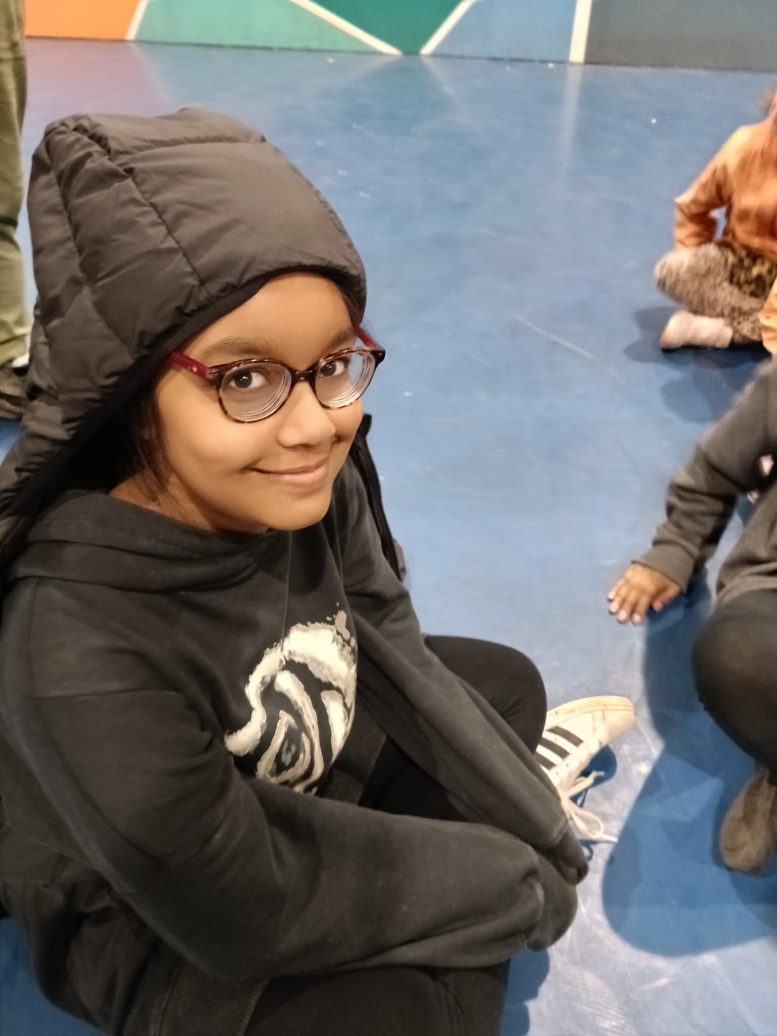A child smiling, sitting on the floor of a sports hall