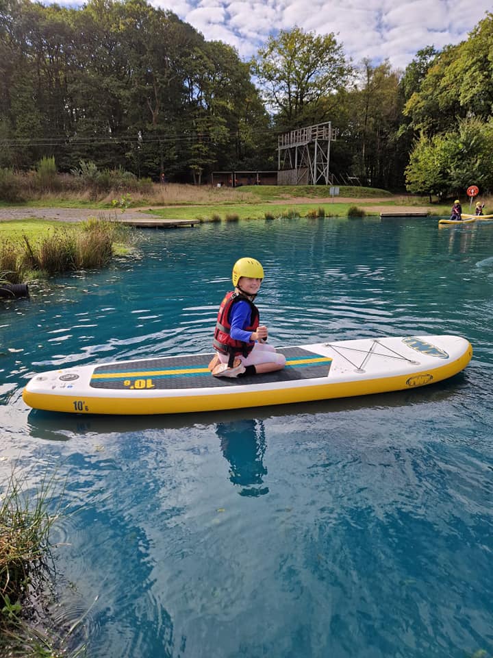 A student kneeling on a paddle board, smiling