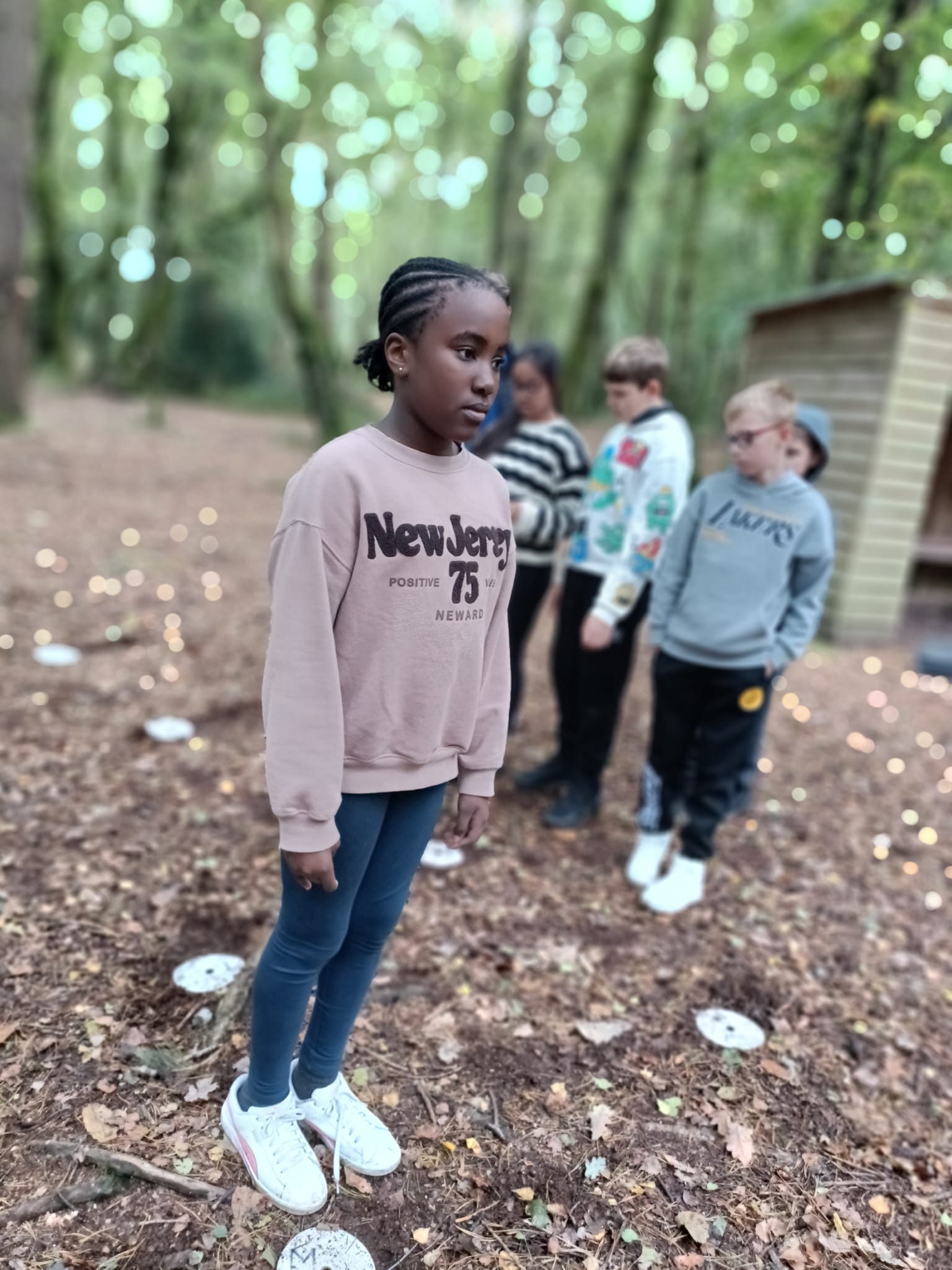 A child in the forest looking to the right, with a group of children behind her