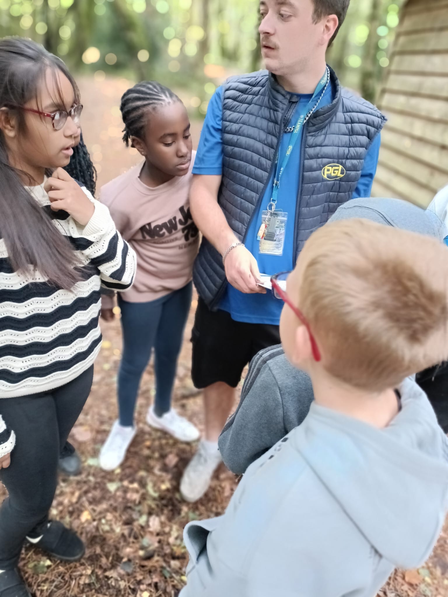 A group of children in a forest, with a PGL instructor, looking at a piece of paper