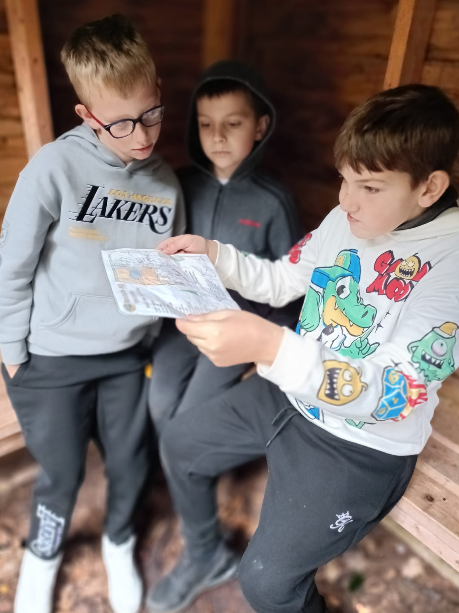 3 children in a wooden hut, looking at a laminated map