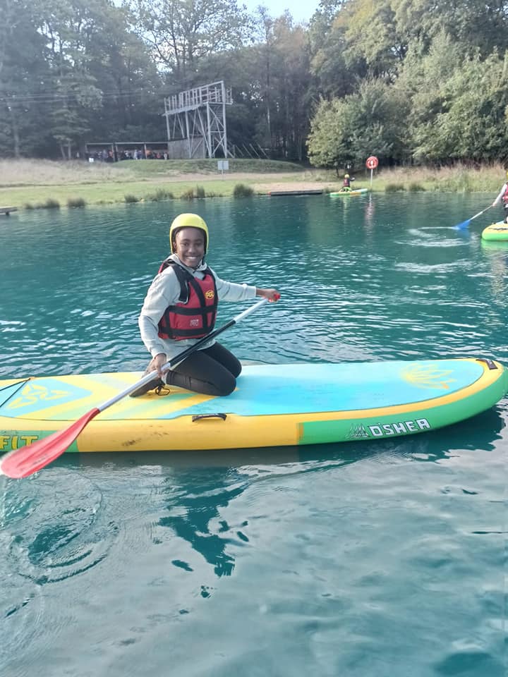 A student kneeling on a paddle board, smiling