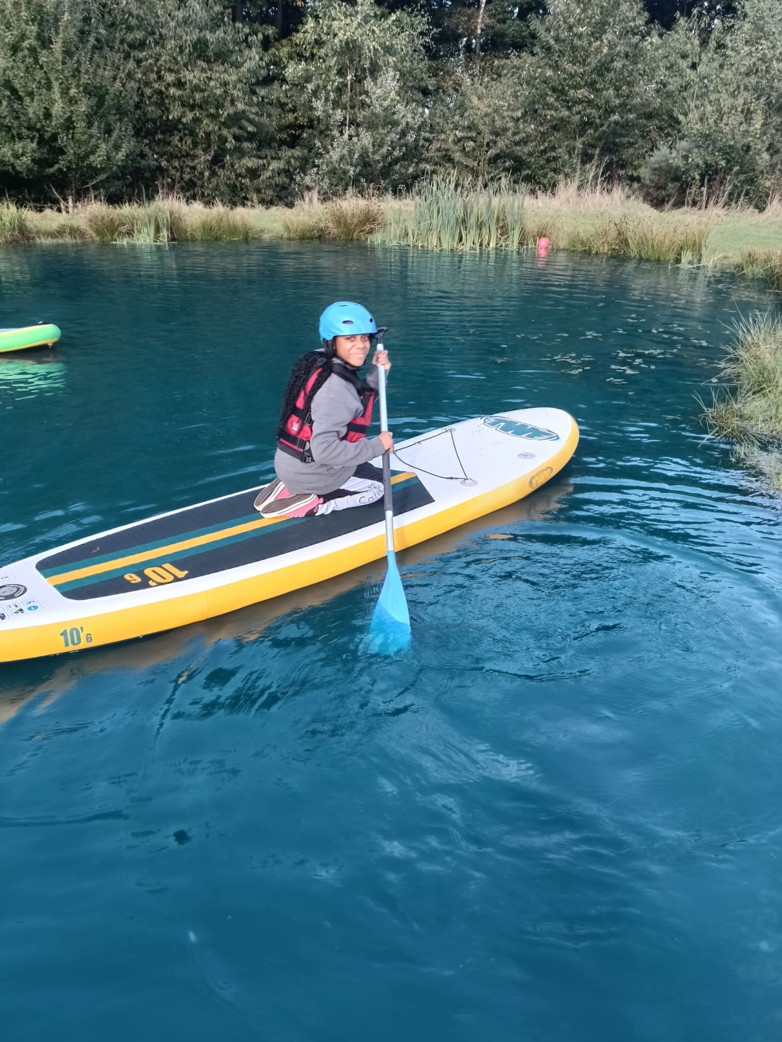 A student kneeling on a paddle board, smiling