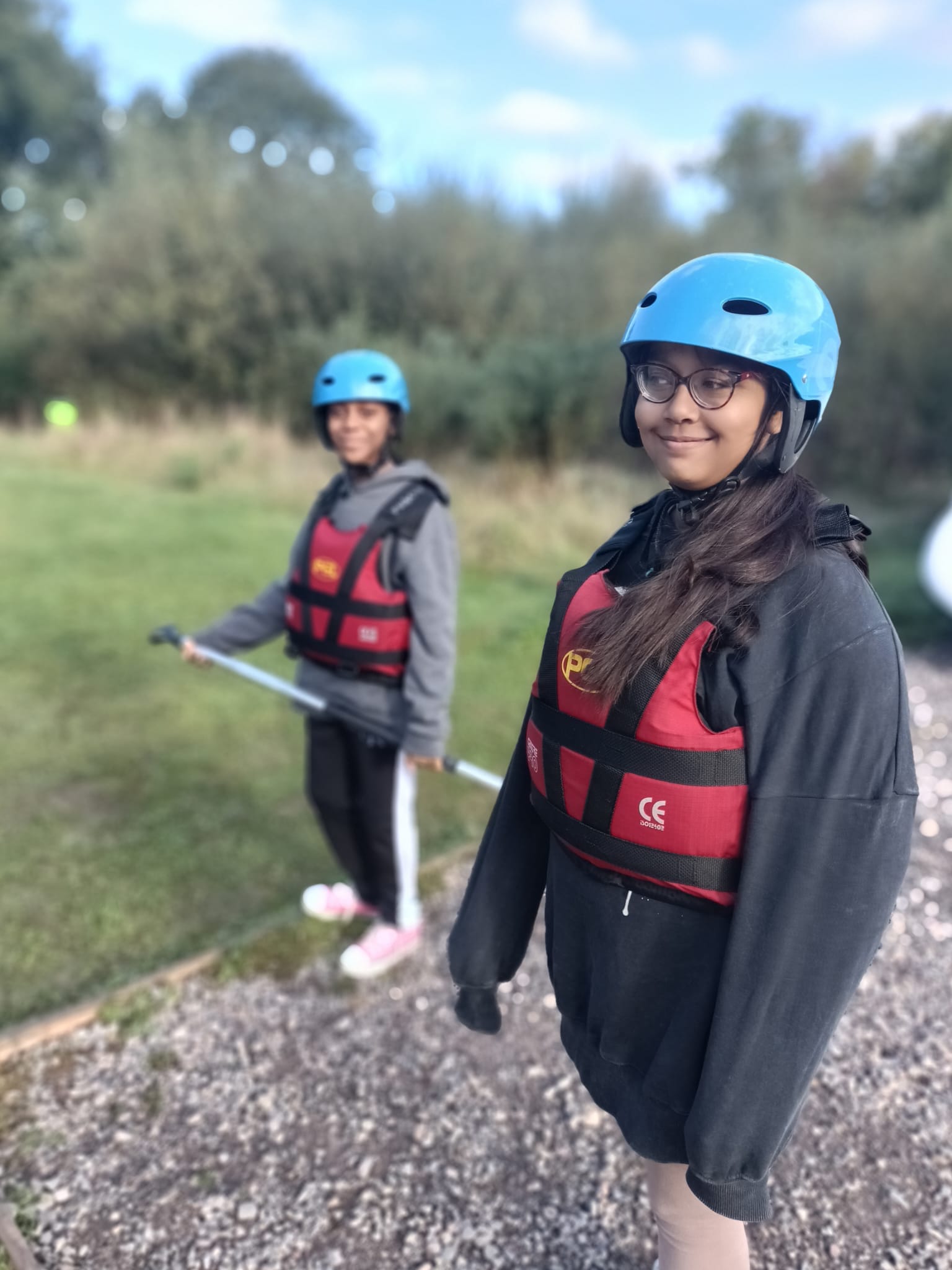 A student in a life jacket and helmet, looking to her right, smiling