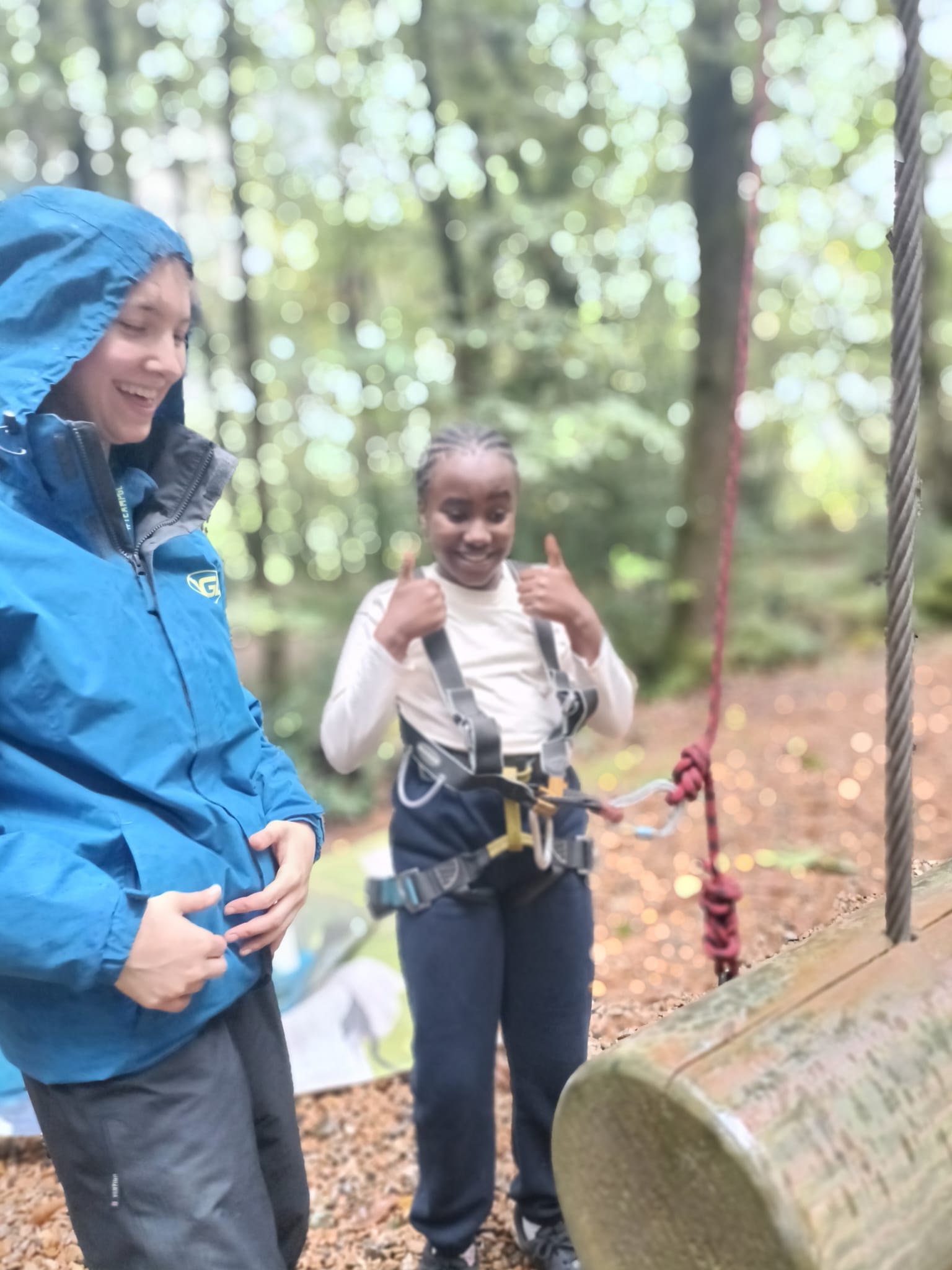 A student in a harness, smiling with their thumbs up, next to a smiling PGL instructor