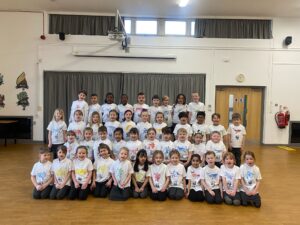 A group of children smiling for a photo, wearing the t-shirts they made